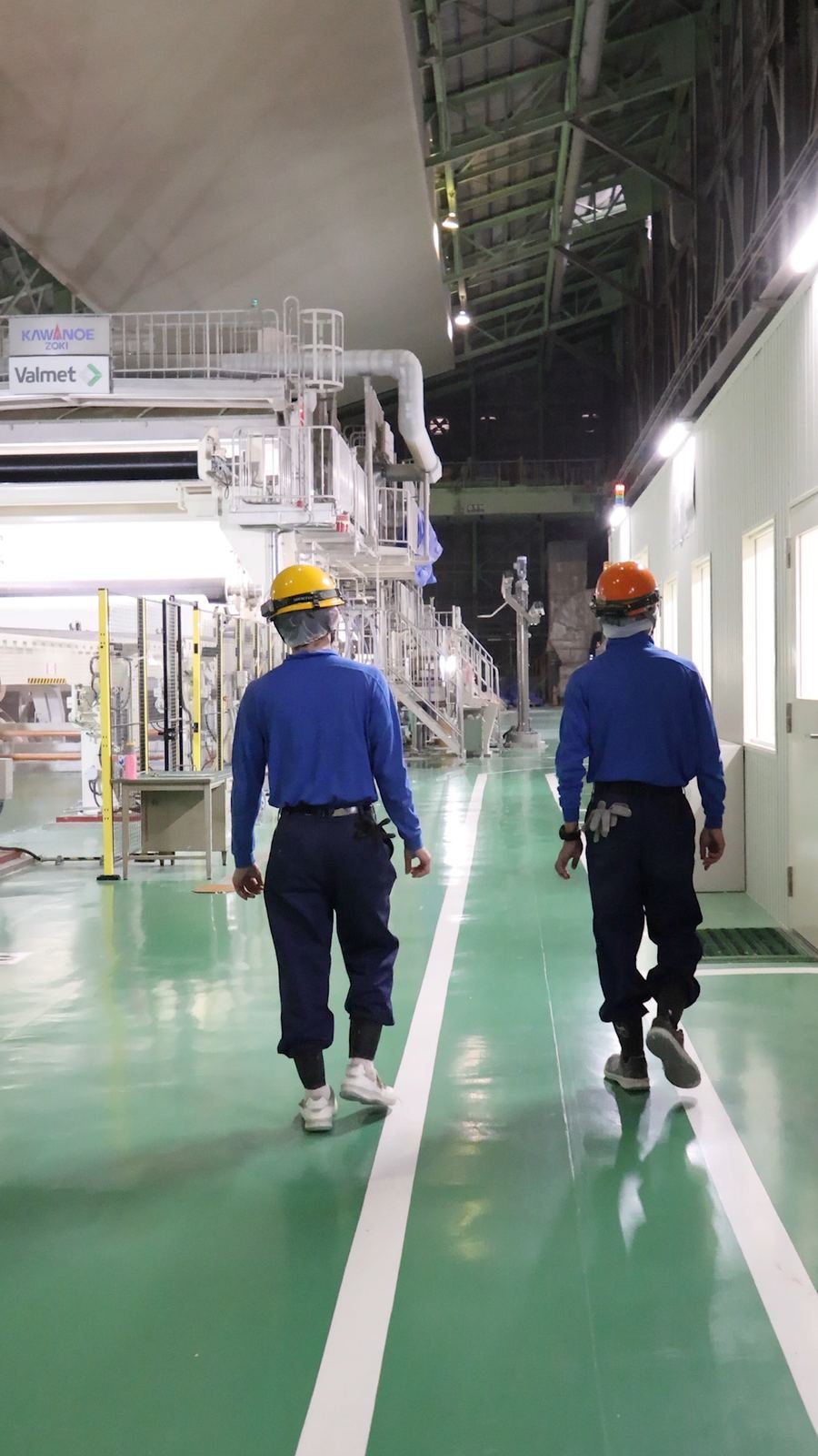 抄紙機の横の通路を歩いて見回る2人の社員